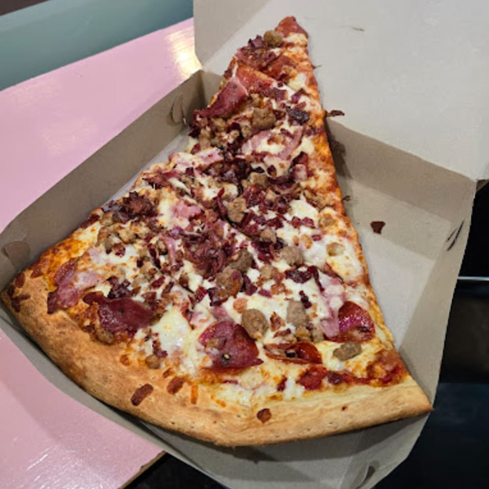 A large slice of Tatiana Pizza's meat lover's pizza, loaded with pepperoni, sausage, and bacon.