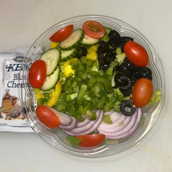 Fresh Italian salad with lettuce, tomatoes, cucumbers, olives, peppers, and red onions in a clear container.