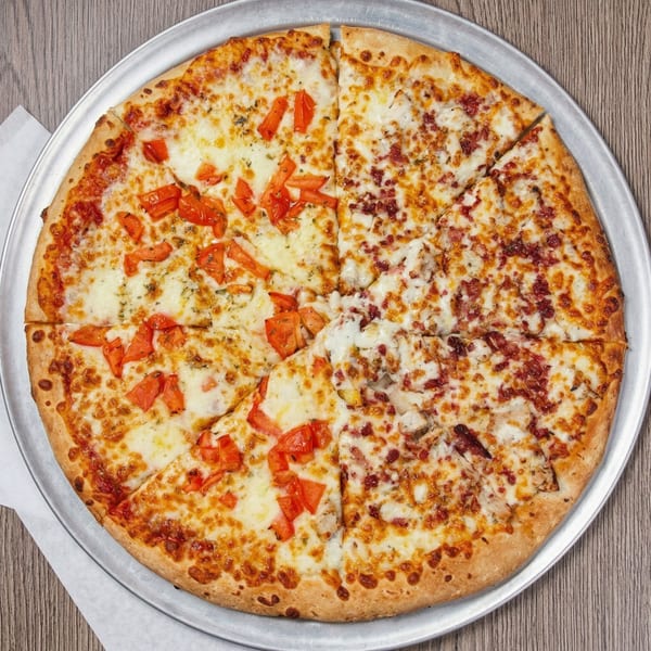 Whole pizza with one half topped with diced tomatoes and the other with bacon and chicken.
