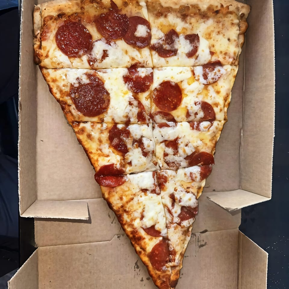 A large, triangular slice of Tatiana Pizza pepperoni pizza, cut into smaller squares, in a cardboard box.