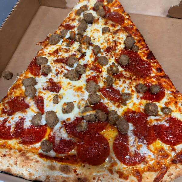 A large slice of Tatiana Pizza with pepperoni, sausage, and melted cheese in a cardboard box.